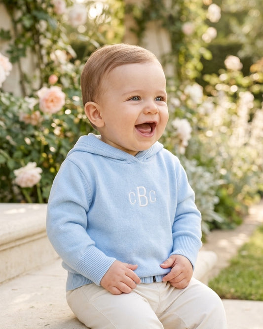 Carriage Boutique baby boy wearing a soft blue cotton hooded sweater with monogram detail in a garden setting