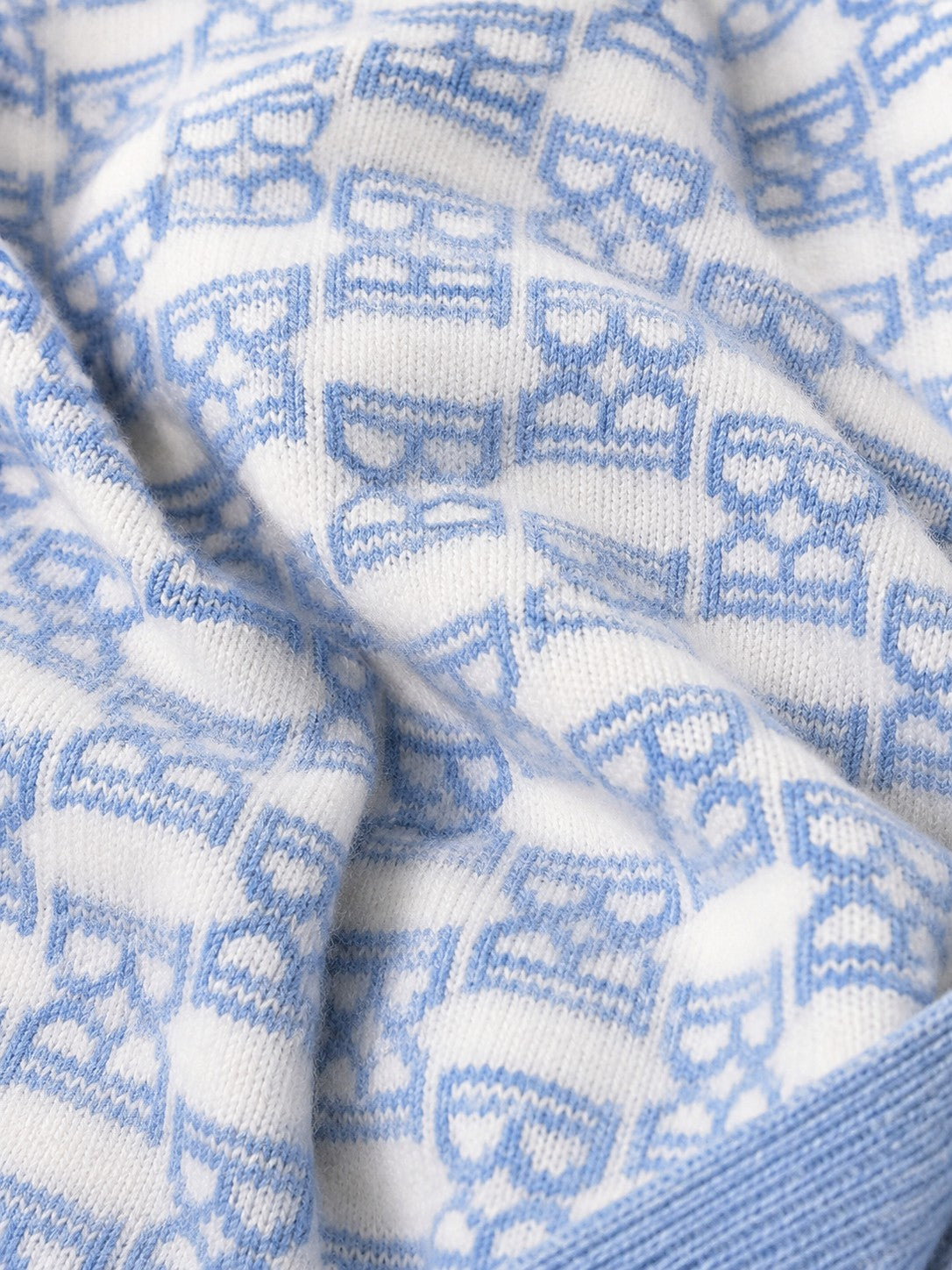 Carriage Boutique baby knit blanket featuring a soft white and blue monogram pattern with a ribbed edge.