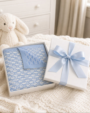 Carriage Boutique blue and white monogram knit baby blanket folded in a gift box with a light blue satin ribbon.