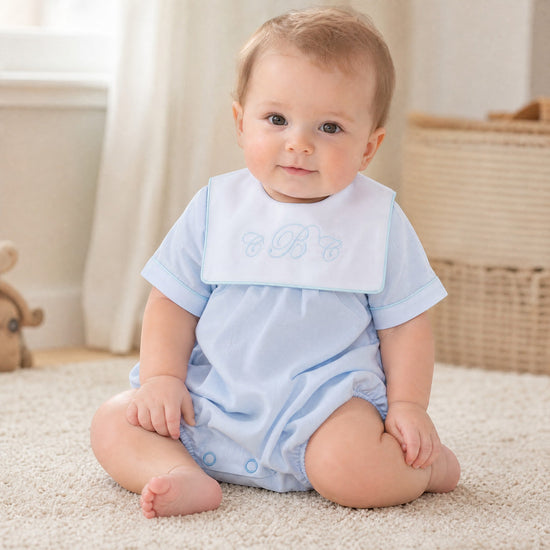 Baby boy wearing a Carriage Boutique light blue cotton romper with a white monogrammed collar sitting on a rug