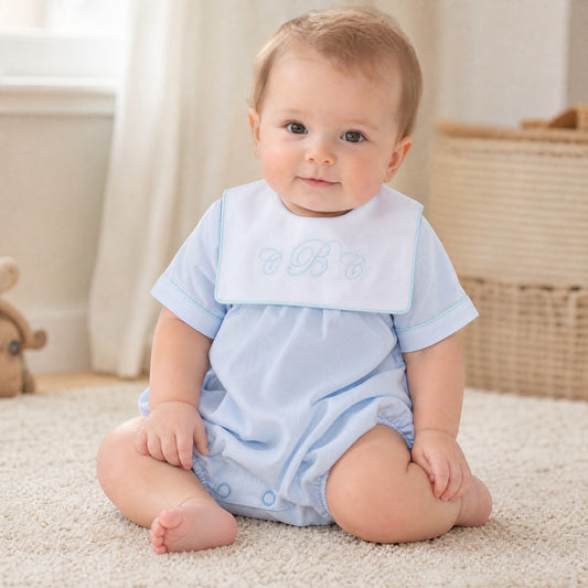 Baby boy wearing a Carriage Boutique light blue cotton romper with a white monogrammed collar sitting on a rug