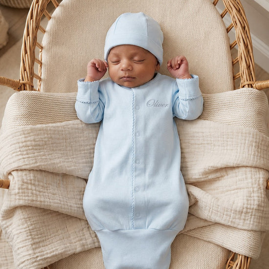 Carriage Boutique blue newborn sleep sack with matching hat and personalized name embroidery in a wicker bassinet