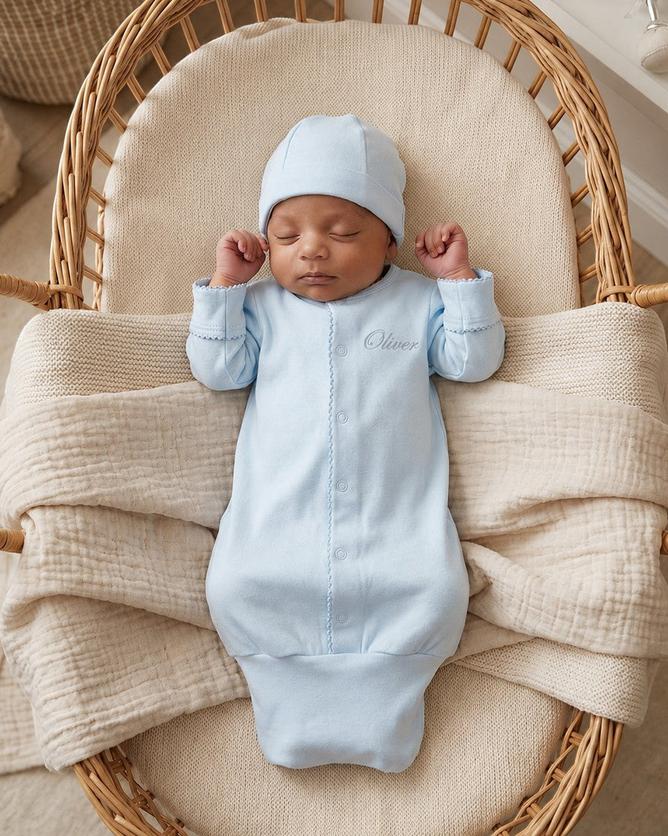 Carriage Boutique blue newborn sleep sack with matching hat and personalized name embroidery in a wicker bassinet