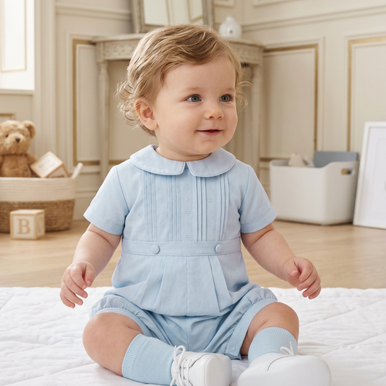 Carriage Boutique baby boy wearing a light blue pique romper with a Peter Pan collar and pleated front detail.