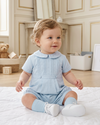 Carriage Boutique baby boy wearing a light blue pique romper with a Peter Pan collar and pleated front detail.