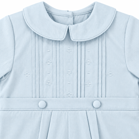 Carriage Boutique baby boy light blue pique romper with a Peter Pan collar, pleated front, and decorative buttons.