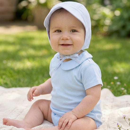 Baby boy wearing a Carriage Boutique blue seersucker sun hat and light blue cotton onesie sitting on a blanket.