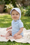 Baby boy wearing a Carriage Boutique blue seersucker sun hat and light blue cotton onesie sitting on a blanket.