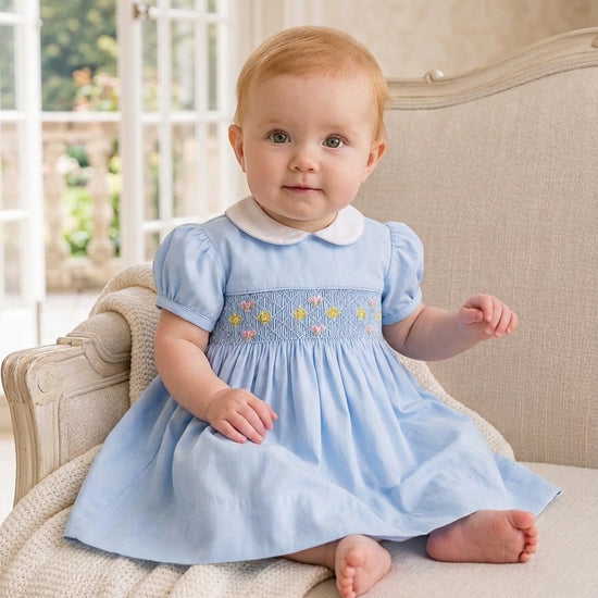 Carriage Boutique baby girl blue dress with hand-smocked waist, floral embroidery, and a white peter pan collar.