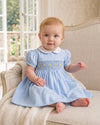 Carriage Boutique baby girl blue dress with hand-smocked waist, floral embroidery, and a white peter pan collar.