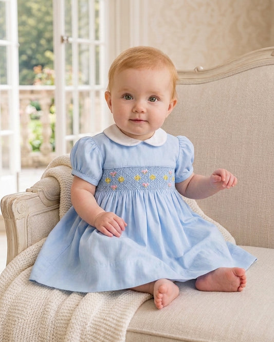 Carriage Boutique baby girl blue dress with hand-smocked waist, floral embroidery, and a white peter pan collar.