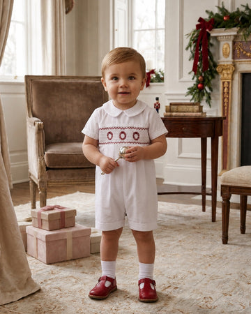Carriage Boutique white batiste boys shortall with hand-smocked holiday wreath detail worn by a toddler