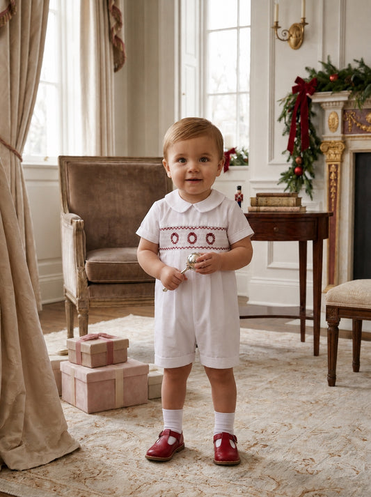 Carriage Boutique white batiste boys shortall with hand-smocked holiday wreath detail worn by a toddler