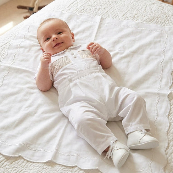 Carriage Boutique white cotton boys christening outfit with hand-smocked detail and satin trim on a baby.