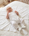 Carriage Boutique white cotton boys christening outfit with hand-smocked detail and satin trim on a baby.