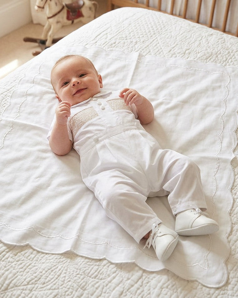 Carriage Boutique white cotton boys christening outfit with hand-smocked detail and satin trim on a baby.