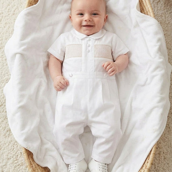 Carriage Boutique white cotton boys christening outfit with hand-smocked detail and satin trim in a wicker basket