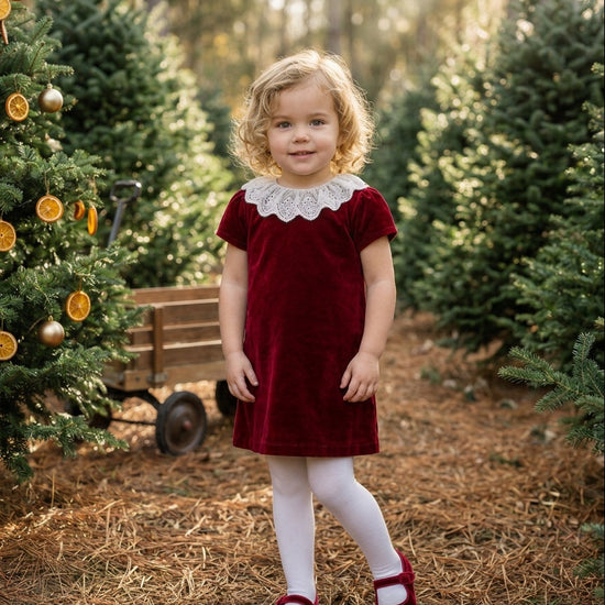 Carriage Boutique burgundy velvet dress with white lace collar worn by a young girl in a Christmas tree farm setting