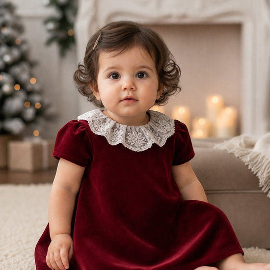 Carriage Boutique burgundy velvet dress for baby girls featuring a delicate white lace collar in a festive setting