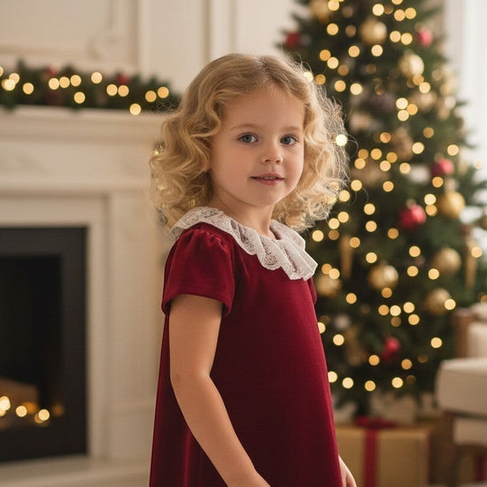 Carriage Boutique burgundy velvet dress with white lace collar worn by a young girl in a festive holiday setting.