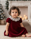 Carriage Boutique burgundy velvet dress with white lace collar worn by a toddler in a festive holiday setting.