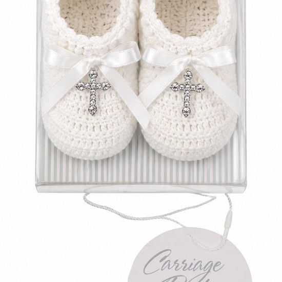 Carriage Boutique white hand-crocheted baby christening shoes with satin bows and gem-adorned cross charms in a box.