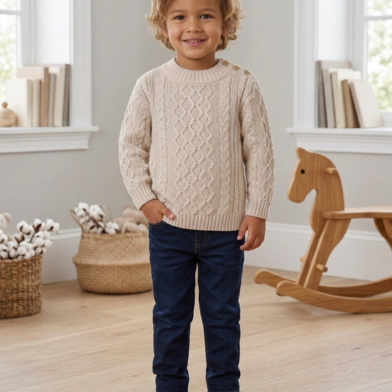 Carriage Boutique beige fisherman knit cotton pullover sweater worn by a smiling toddler boy with jeans and boots