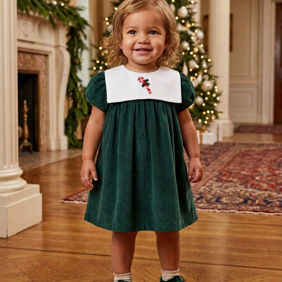 Carriage Boutique toddler girl wearing a green corduroy holiday dress with a white smocked bib and candy cane detail.