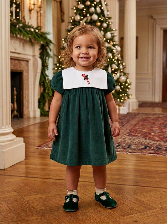 Carriage Boutique toddler girl wearing a green corduroy holiday dress with a white smocked bib and candy cane detail.