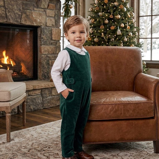 Carriage Boutique baby boy wearing a green velvet long romper over a white collared shirt by a Christmas tree.