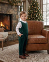 Carriage Boutique baby boy wearing a green velvet long romper over a white collared shirt by a Christmas tree.