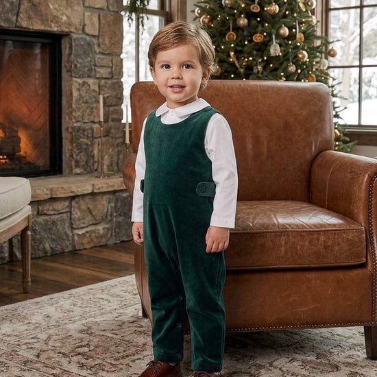 Carriage Boutique baby boy wearing a green velvet long romper over a white collared shirt in a cozy living room.