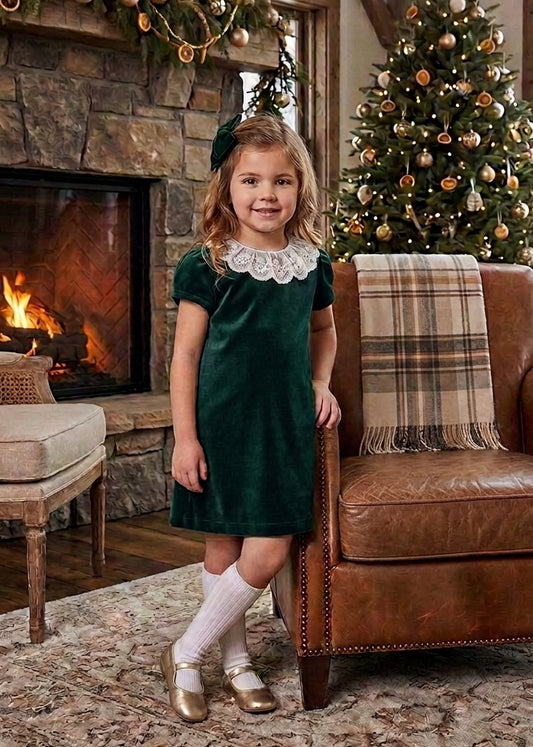 Carriage Boutique toddler girl in a green velvet dress with a white lace collar standing by a Christmas tree
