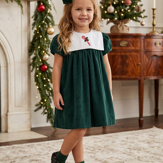 Carriage Boutique toddler girl wearing a dark green velvet holiday dress with a white bib and candy cane embroidery.