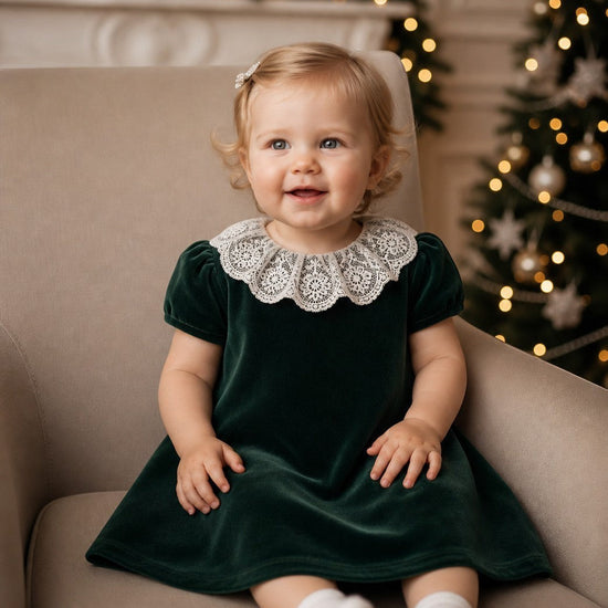 Carriage Boutique green velvet dress with white lace collar worn by a toddler sitting in a chair by a Christmas tree