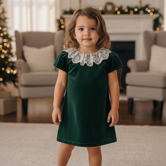 Carriage Boutique toddler girl wearing a green velvet dress with a delicate white lace collar in a festive room.