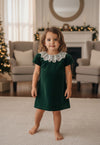 Carriage Boutique toddler girl wearing a green velvet dress with a delicate white lace collar in a festive room.