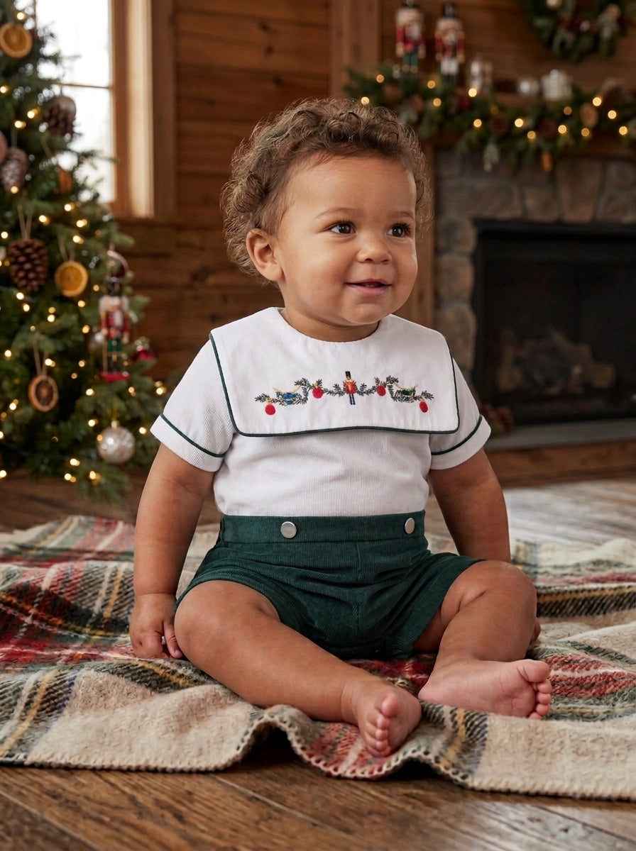 Carriage Boutique infant boy wearing a green and white smocked bobbie suit with a wooden soldier motif on a blanket.