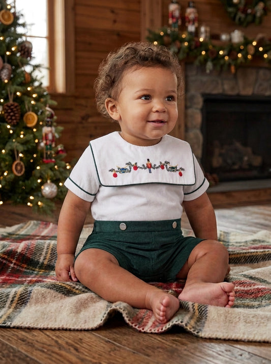 Carriage Boutique infant boy wearing a green and white smocked bobbie suit with a wooden soldier motif on a blanket.