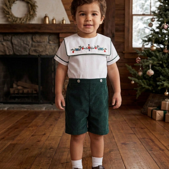 Toddler boy wearing a Carriage Boutique green corduroy shorts and white smocked shirt with wooden soldier embroidery.