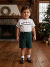 Toddler boy wearing a Carriage Boutique green corduroy shorts and white smocked shirt with wooden soldier embroidery.