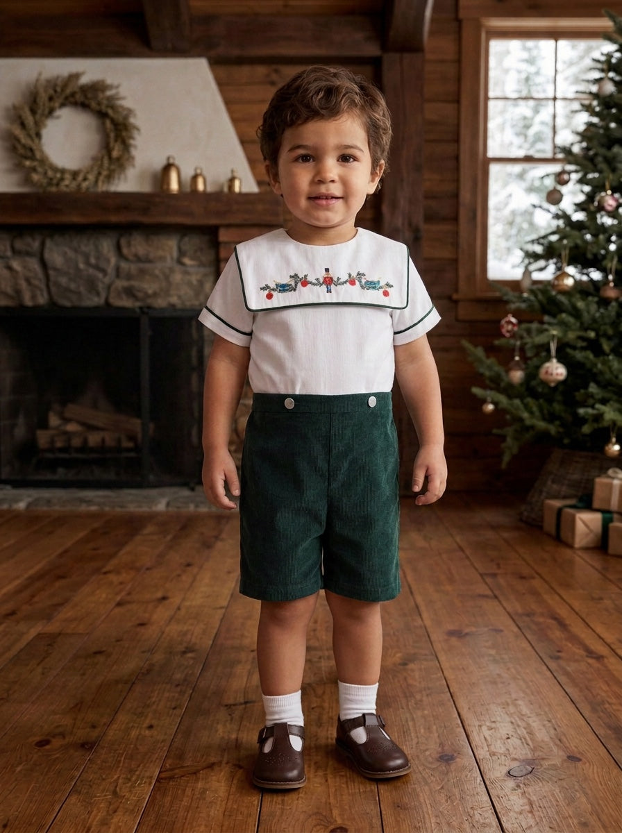 Toddler boy wearing a Carriage Boutique green corduroy shorts and white smocked shirt with wooden soldier embroidery.