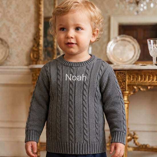 Carriage Boutique grey cable-knit cotton sweater with Noah monogram on chest worn by a toddler boy