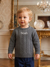 Carriage Boutique grey cable-knit cotton sweater with Noah monogram on chest worn by a toddler boy