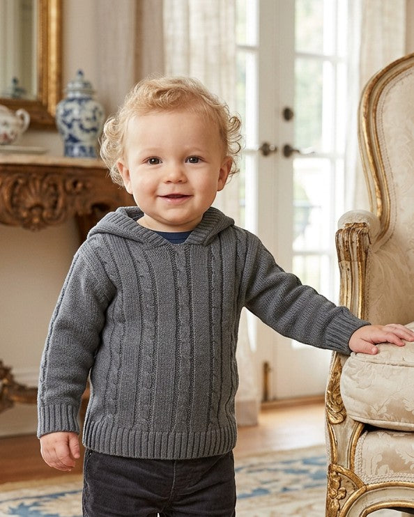 Carriage Boutique baby boy wearing a dark grey cable-knit hooded sweater with ribbed cuffs in a classic room setting.