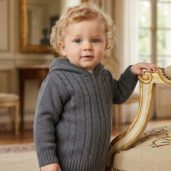 Carriage Boutique baby boy wearing a dark grey cable-knit cotton sweater with a hood and ribbed cuffs.