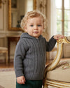 Carriage Boutique baby boy wearing a dark grey cable-knit cotton sweater with a hood and ribbed cuffs.