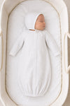 Newborn sleeping in a Carriage Boutique white gown and bonnet set with a grey star print in a bassinet.