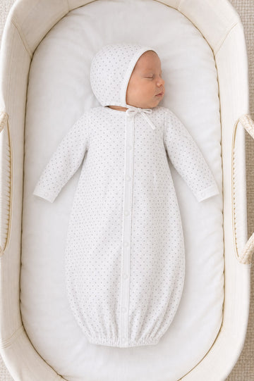 Newborn sleeping in a Carriage Boutique white gown and bonnet set with a grey star print in a bassinet.