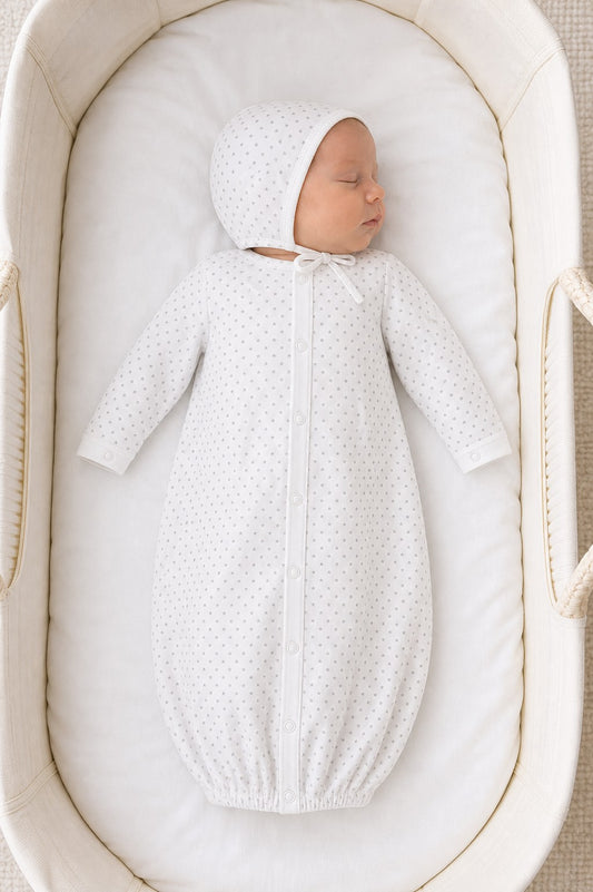 Newborn sleeping in a Carriage Boutique white gown and bonnet set with a grey star print in a bassinet.